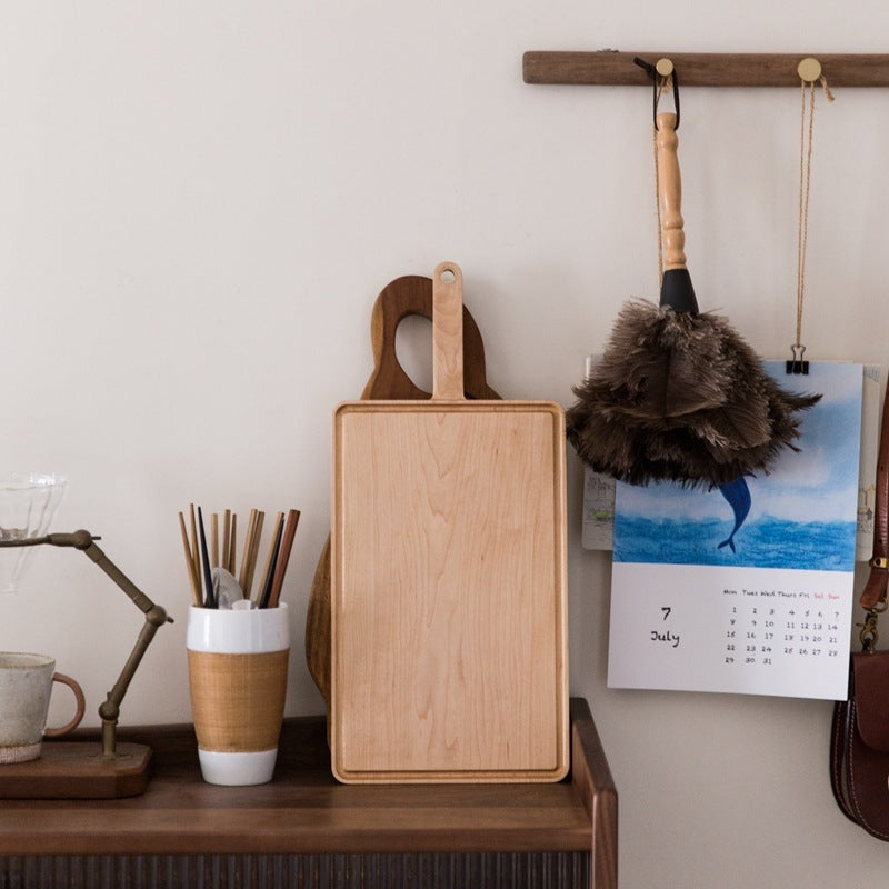 The Maple Wooden Cutting Board standing vertically on a desk, showing off its wood grain and light natural wood color.
