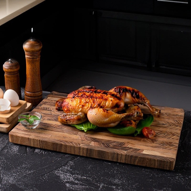 The Walnut Wood Chopping Board with a whole chicken on it, with tomatoes and basil.