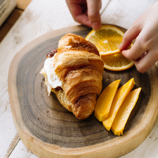 The Acacia Wood Log Cutting Board with croissants and lemons on it.