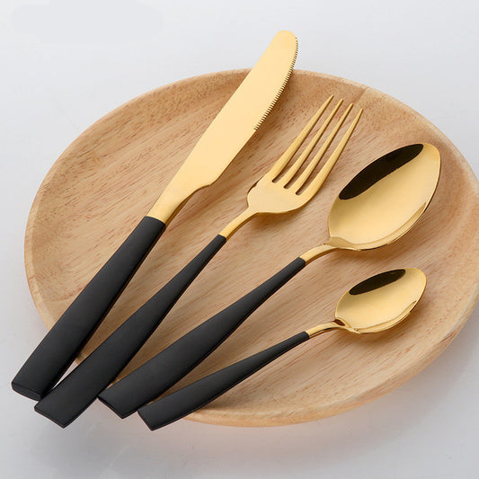 The Black and Gold Stainless Steel Four-Piece Cutlery Set on a bamboo plate.