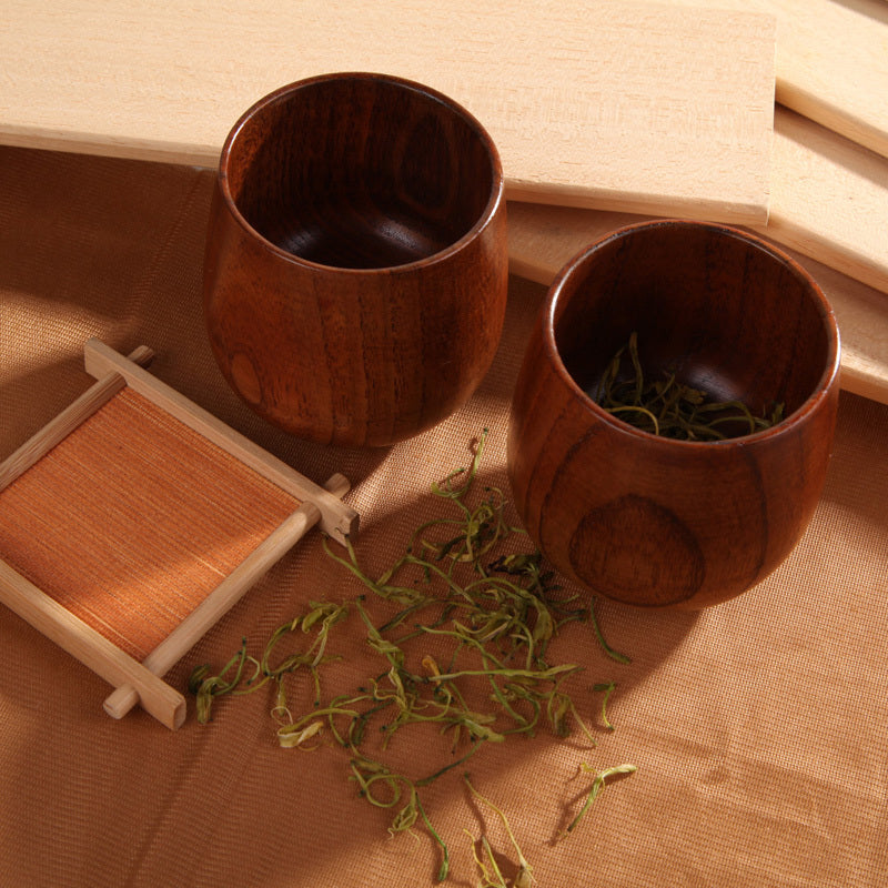 The Handmade Jujube Wooden Tea Cup with green leaves in and around the tea cups.