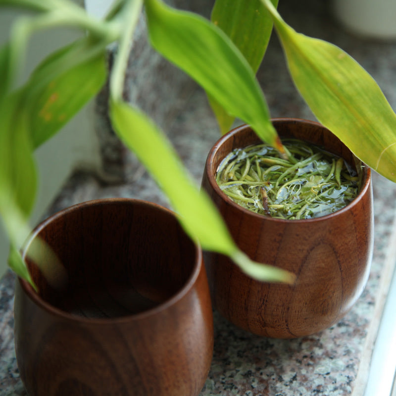 The Handmade Jujube Wooden Tea Cup with tea and green leaves in the tea.