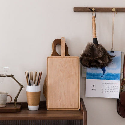 The Maple Wooden Cutting Board standing vertically on a desk, showing off its wood grain and light natural wood color.