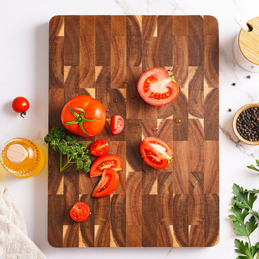 The Rectangular Acacia End-Grain Cutting Board with tomatoes cut in half on it.