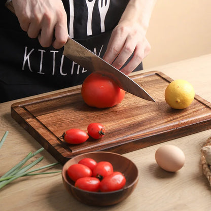 The small Acacia Thick One-Piece Wood Cutting Board with a large tomatoe being cut on it.