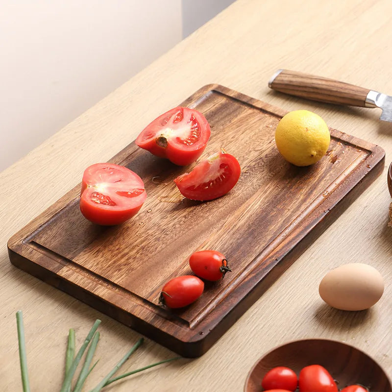 The small Acacia Thick One-Piece Wood Cutting Board with tomatoes being cut on it.