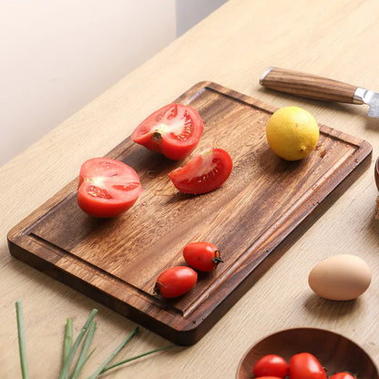 The small Acacia Thick One-Piece Wood Cutting Board with tomatoes being cut on it.
